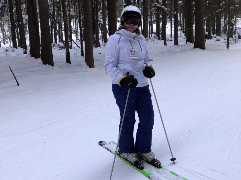 A woman in white jacket skiing on snow covered ground.