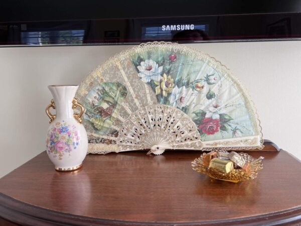 A vase and fan on the table in front of a television.