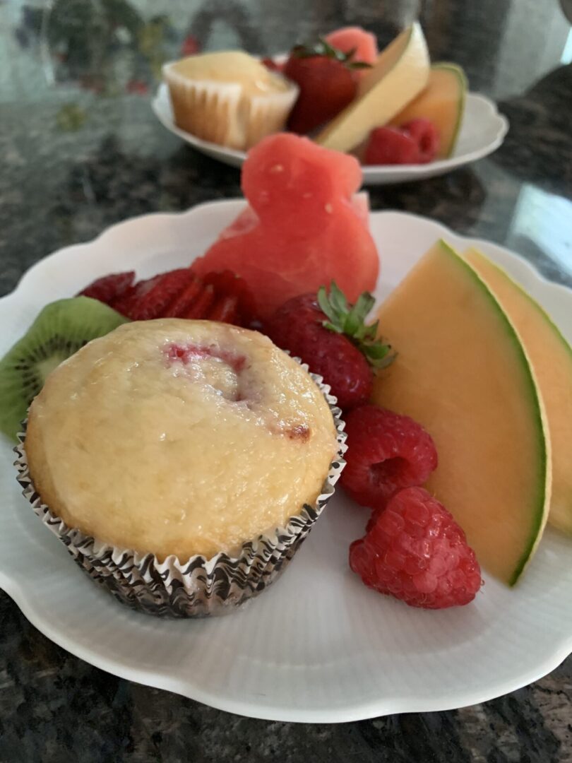 A plate of fruit and muffins on the table.