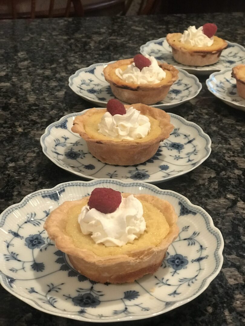 A group of small pies on plates with whipped cream and strawberries.