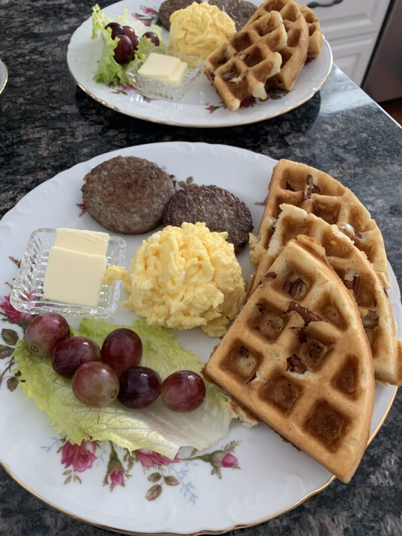 A plate of food with waffles, grapes and butter.