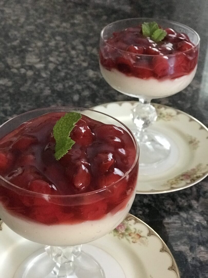 Two glasses of dessert with cherries on top.